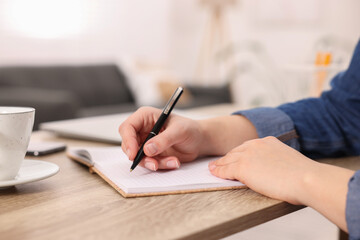 Young woman writing in notebook at wooden table, closeup - obrazy, fototapety, plakaty