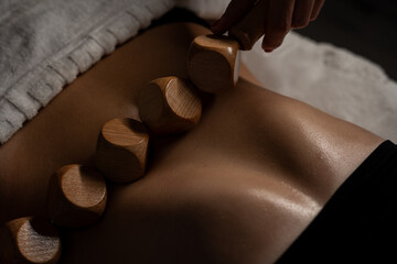 Anti-cellulite massage on the stomach using wooden objects. Massage salon in a dark room. - obrazy, fototapety, plakaty
