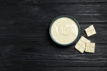 Tasty white chocolate paste in bowl and pieces on black wooden table, top view. Space for text