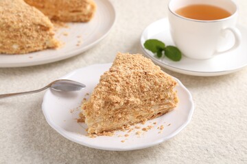 Piece of delicious Napoleon cake served on beige table, closeup