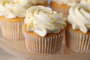 Delicious cupcakes with white cream and lemon zest on plate, closeup