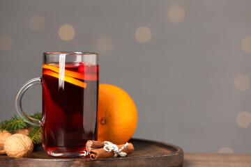 Aromatic mulled wine in glass cup on table against grey background with blurred lights, closeup....