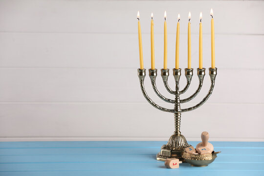 Hanukkah celebration. Menorah with burning candles and dreidels on light blue wooden table, space for text