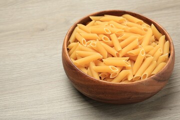 Raw penne pasta in bowl on light grey wooden table, closeup. Space for text