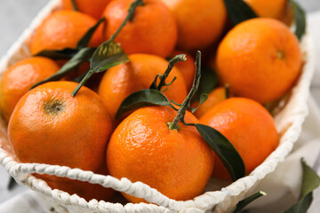 Fresh ripe tangerines and leaves in basket on table, closeup