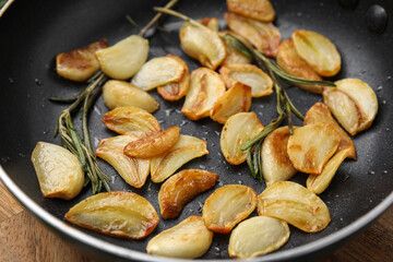 Frying pan with fried garlic cloves and rosemary, closeup