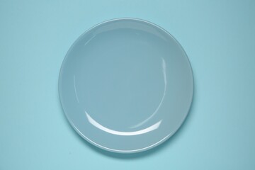 One ceramic plate on light blue background, top view