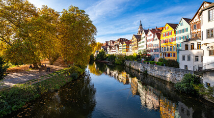 Panoramic view of famous historic facades of old town of Tuebingen on Neckar River in southern Germany. Autumn season atmosphere with colorful foliage, Hölderlin tower and church. Sunny blue sky day. - obrazy, fototapety, plakaty