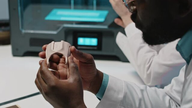 Female engineer taking out new part of prosthetic from 3D printer and her male partner taking good look at its qualityFemale engineer taking out new part of prosthetic from 3D printer and her male par