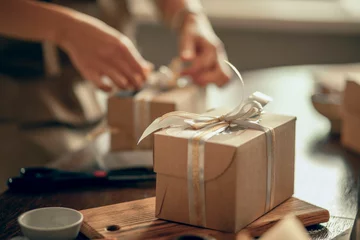 Foto op Canvas A craft box with white and gold ribbons. A woman's hands ties a ribbon on a customer's order box. A small business entrepreneur and the concept of food delivery. © Айман Дайрабаева