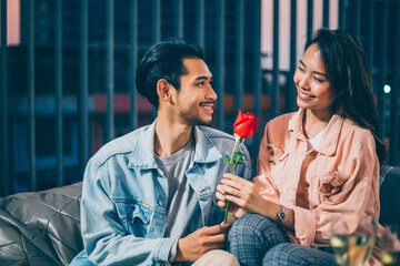 Asian man giving roses to propose his girlfriend on rooftop at night, focus on happy surprise woman...