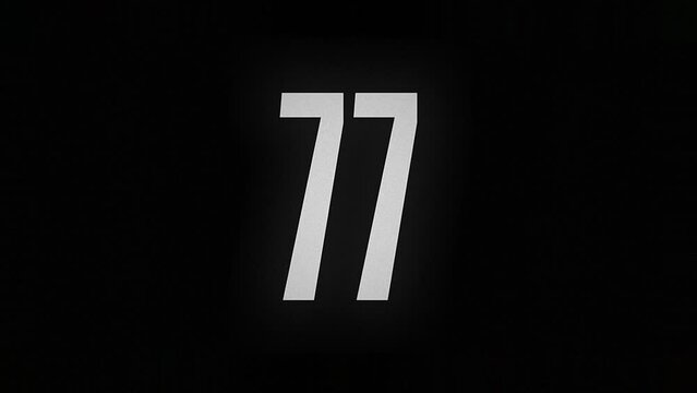 The number 77 smolders and burns on a black background, the number is on fire