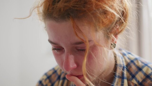 Close up of redheaded girl with tied up hair crying while speaking some words. Handheld