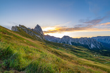 Golden sunrise at Seceda, Dolomites, Italy, A breathtaking spectacle unfolds, casting warm hues on the rugged landscape and meadows, creating a serene and radiant morning panorama.
