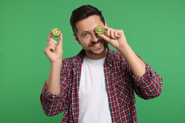 Man holding halves of kiwi on green background - obrazy, fototapety, plakaty