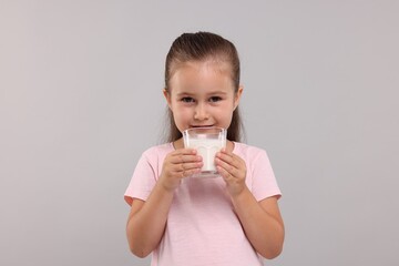 Cute girl with glass of fresh milk on light grey background