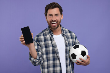 Happy sports fan with soccer ball and smartphone on purple background