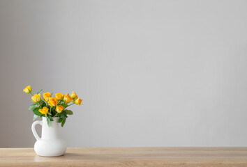 yellow roses in white jug on wooden shelf