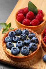 Tartlets with different fresh berries on wooden board, closeup. Delicious dessert
