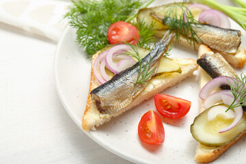 Delicious sandwiches with sprats, pickled cucumber, onion and dill served on white wooden table, closeup