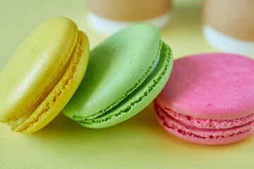 Multicolored macaroons on a yellow background with coffee in cups.