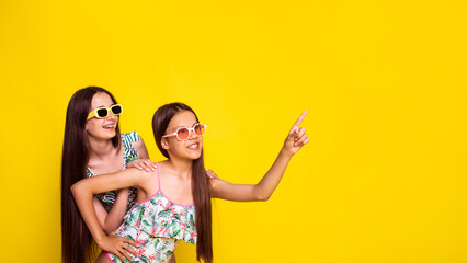 two teen girls looking to side and point hand on free place for text on yellow background