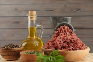 Mincing beef with manual meat grinder. Parsley, oil and spices on wooden table