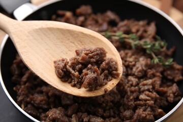 Holding spoon with fried ground meat over frying pan, closeup