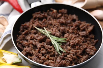 Fried ground meat in frying pan and rosemary on white table, closeup