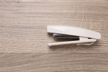 One beige stapler on wooden table, top view. Space for text