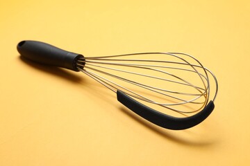 Metal whisk on yellow background, closeup. Kitchen tool