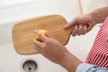 Man rubbing wooden cutting board with lemon at sink in kitchen, closeup