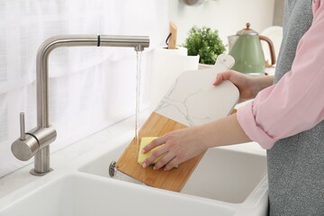 Woman washing cutting board at sink in kitchen, closeup