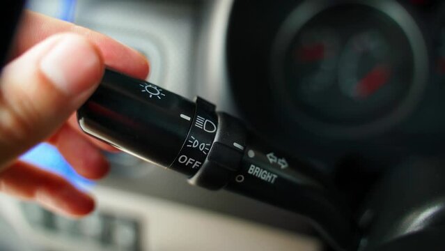A hand switches the headlight modes of a car, close-up. High beam and running lights on the switch in the car interior