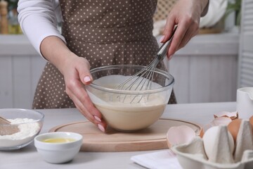 Woman making dough with whisk in bowl at table, closeup