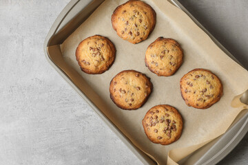 Baking pan with chocolate chip cookies on gray table, top view. Space for text
