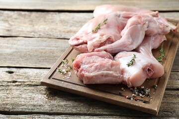 Fresh raw rabbit meat and spices on wooden table, space for text
