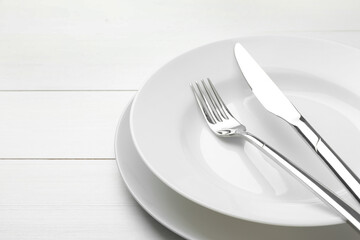 Clean plates, fork and knife on white wooden table, closeup. Space for text
