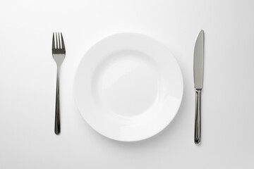 Empty plate, fork and knife on white background, top view