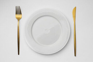 Empty plate, fork and knife on white background, top view