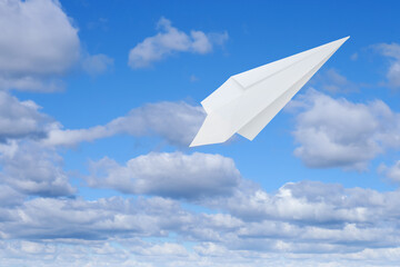 White paper plane flying in blue sky with clouds with clouds