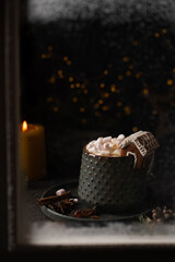 Hot winter drink in a clay mug behind the window. Close-up of hot chocolate with gingerbread house....