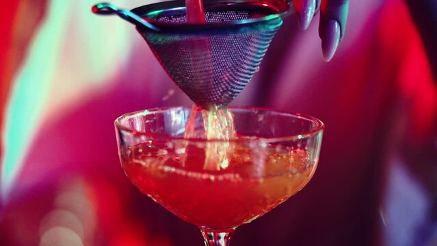 Young girl, bartender pouring cocktail from steel shaker. Making delicious cocktails in neon bar. Concept of occupation, nightlife, bar, party, alcohol drink, mixologist
