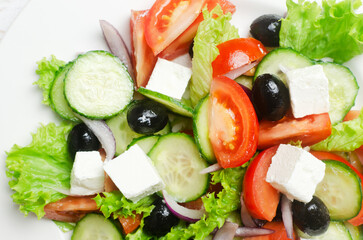 Classic Greek salad with cucumbers, tomatoes, red onion, feta cheese, lettuce and black olives on a white wooden table. The concept of traditional dishes. Simple ingredients. Top view.