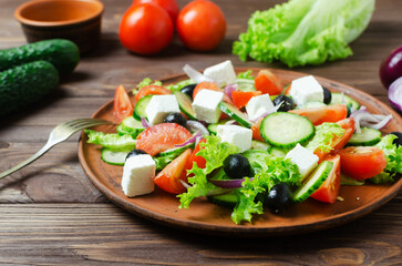 Classic Greek salad with cucumbers, tomatoes, red onion, feta cheese, lettuce and black olives on a wooden table. The concept of traditional dishes. Bossage. Simple ingredients. Top view.