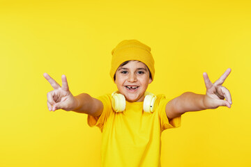 Joyful young boy in yellow clothes and hat, flashing peace signs with a cheerful smile, isolated on...