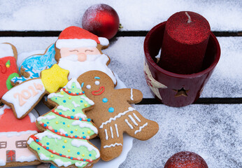 A plate full of Christmas gingerbread cookies on a table covered with snow and Christmas decorations.