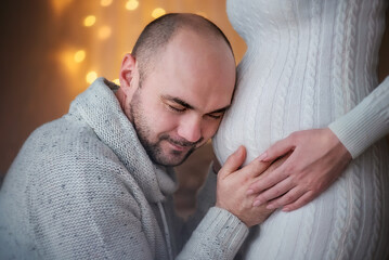 A guy hugs the belly of a pregnant girl. Young family. Husband and wife expecting a baby. Pregnancy. Tenderness. Portrait of a father. New Year. Christmas. Winter. 
