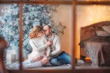 Young family. The guy and the girl look at each other. Husband and wife expecting a baby. Pregnancy. Tenderness. The girl touched the guy's face. Waiting for Christmas. New Year. Christmas. Winter. 