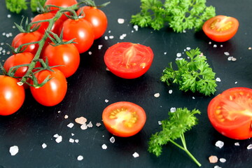 Red cherry tomatoes sprinkled with coarse salt lie on a black background.	